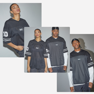 To modeller poserer i sorte oversized fodboldtrøjer med hvide striber på ærmerne og tallet "10" trykt på det ene ærme. Trøjerne har et lille hvidt logo på brystet, og modellerne er stylet afslappet med minimale accessories. Baggrunden er neutral, så fokus forbliver på de streetwear-inspirerede outfits.